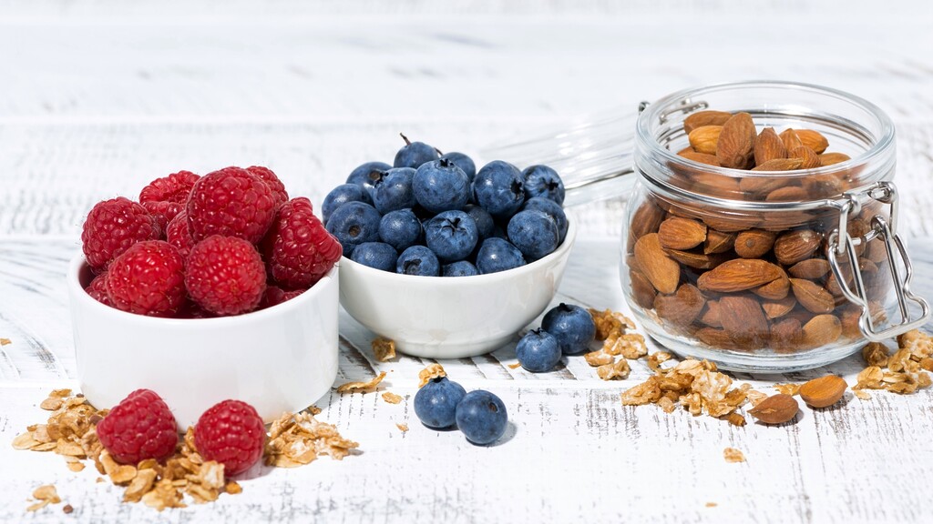 Bowls of raspberries and blueberries served with a jar of almonds.