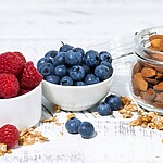 Bowls of raspberries and blueberries served with a jar of almonds.