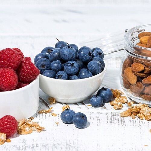 Bowls of raspberries and blueberries served with a jar of almonds.