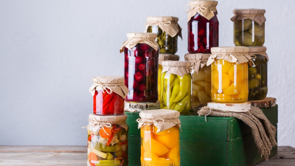 Assorted jars of pickled and fermented vegetables arranged on a rustic green wooden crate.