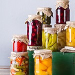 Assorted jars of pickled and fermented vegetables arranged on a rustic green wooden crate.