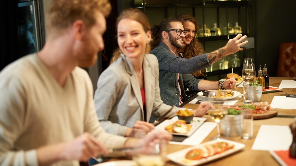 Friends enjoying dinner together at a restaurant while one person takes a selfie at the table.