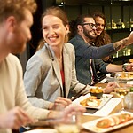 Friends enjoying dinner together at a restaurant while one person takes a selfie at the table.