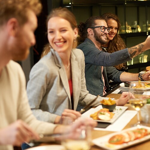 Friends enjoying dinner together at a restaurant while one person takes a selfie at the table.