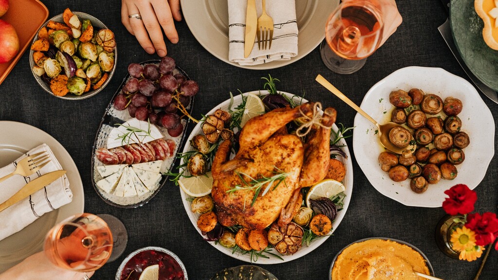 Holiday dinner table with roast turkey, vegetables, mushrooms, grapes, cheese, and wine.