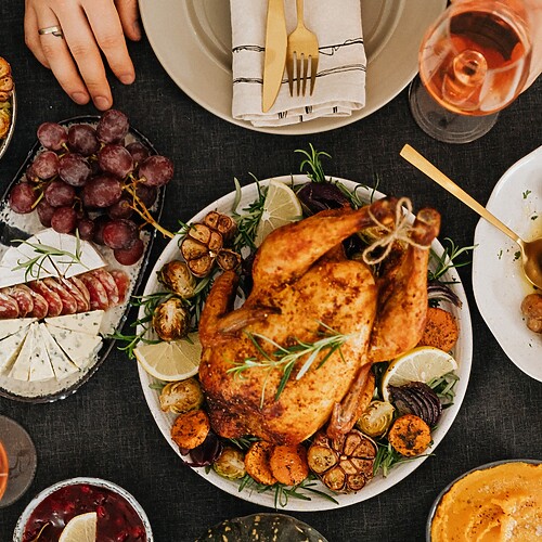 Holiday dinner table with roast turkey, vegetables, mushrooms, grapes, cheese, and wine.