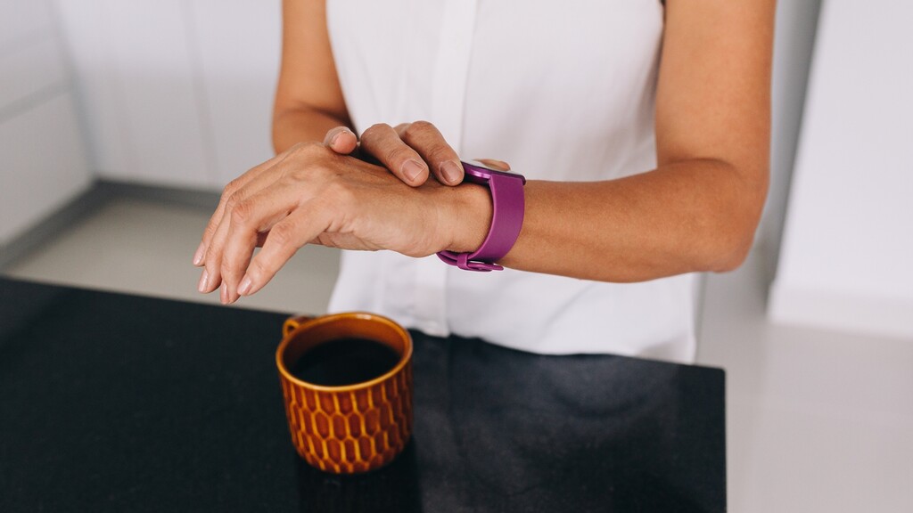 Woman checking her smartwatch beside a cup of black coffee during a morning fasting routine.