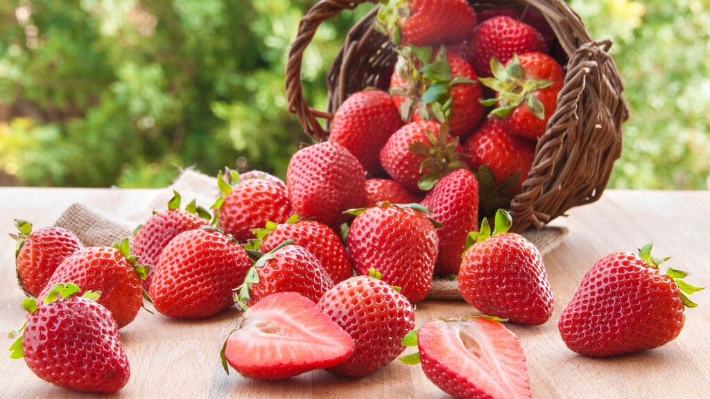 Fresh strawberries spilling from a wicker basket onto a wooden surface.