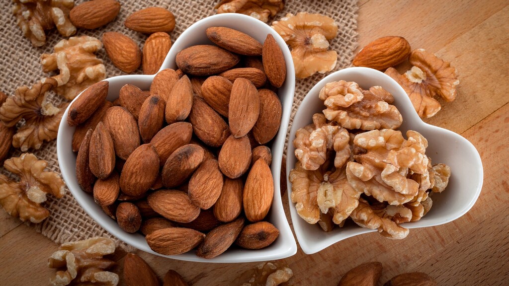 Almonds and walnuts served in small white bowls on a wooden surface.