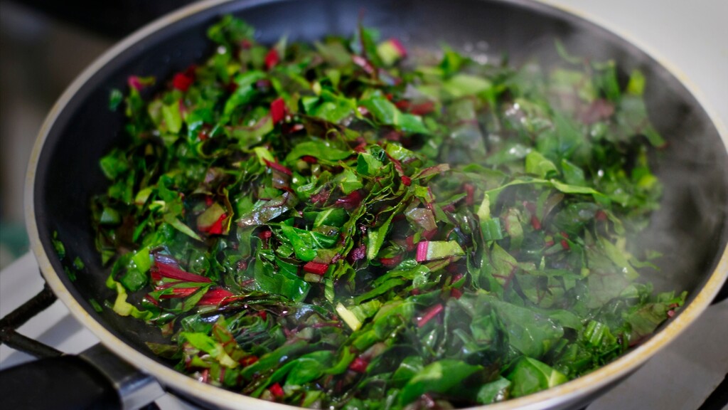 Spinach and Swiss chard sautéing in a pan with steam rising.