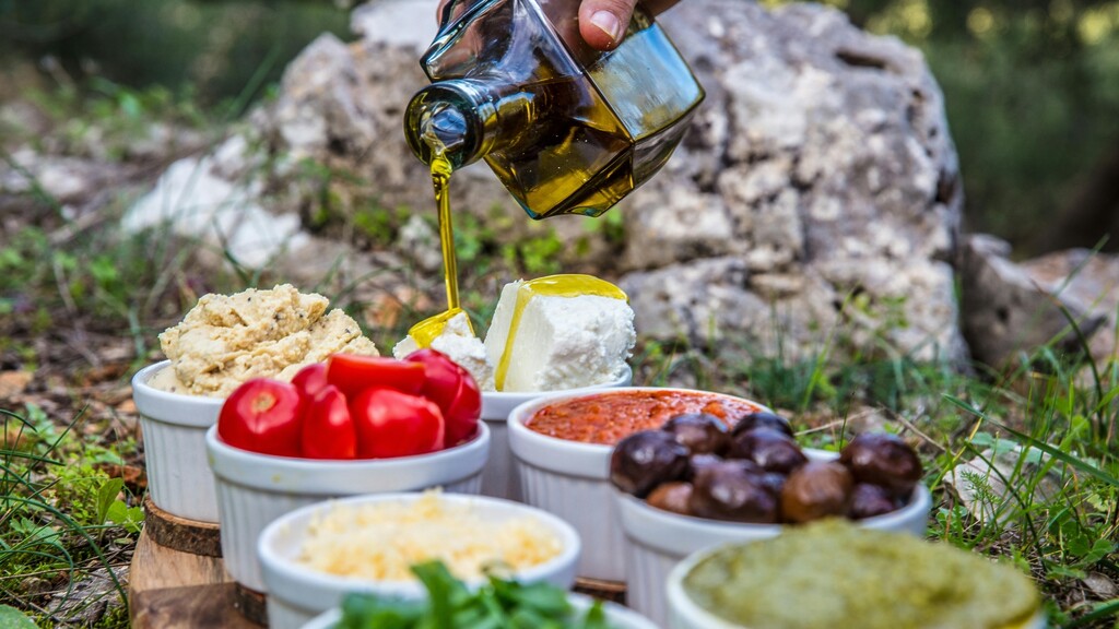 Extra virgin olive oil being poured over Mediterranean-style appetizers.