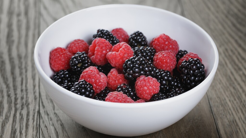 Fresh raspberries and blackberries in a white bowl on a wooden table.