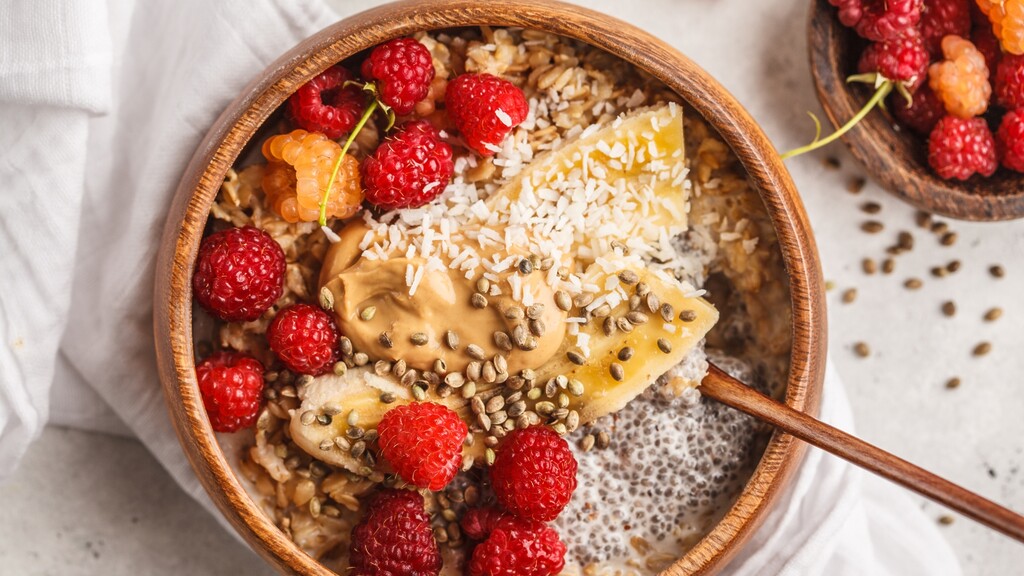Oatmeal bowl topped with raspberries, banana, seeds, coconut, and peanut butter.