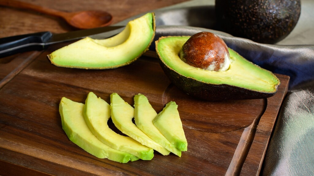 Sliced avocado halves on a wooden cutting board with a kitchen knife.