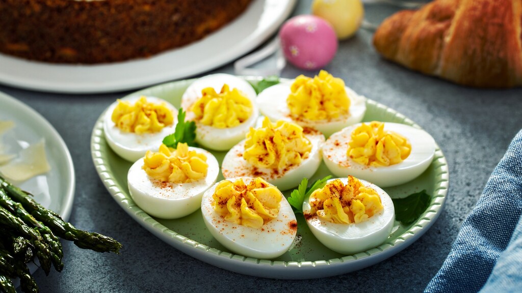 Deviled eggs sprinkled with paprika on a green plate beside brunch dishes.
