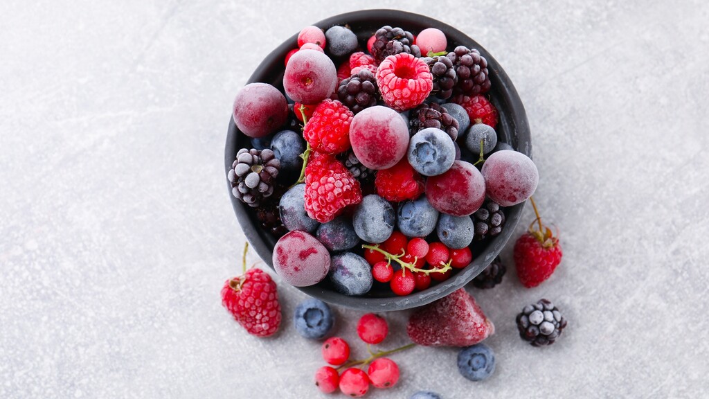 Bowl of mixed berries with raspberries, blueberries, blackberries, and grapes on a light surface