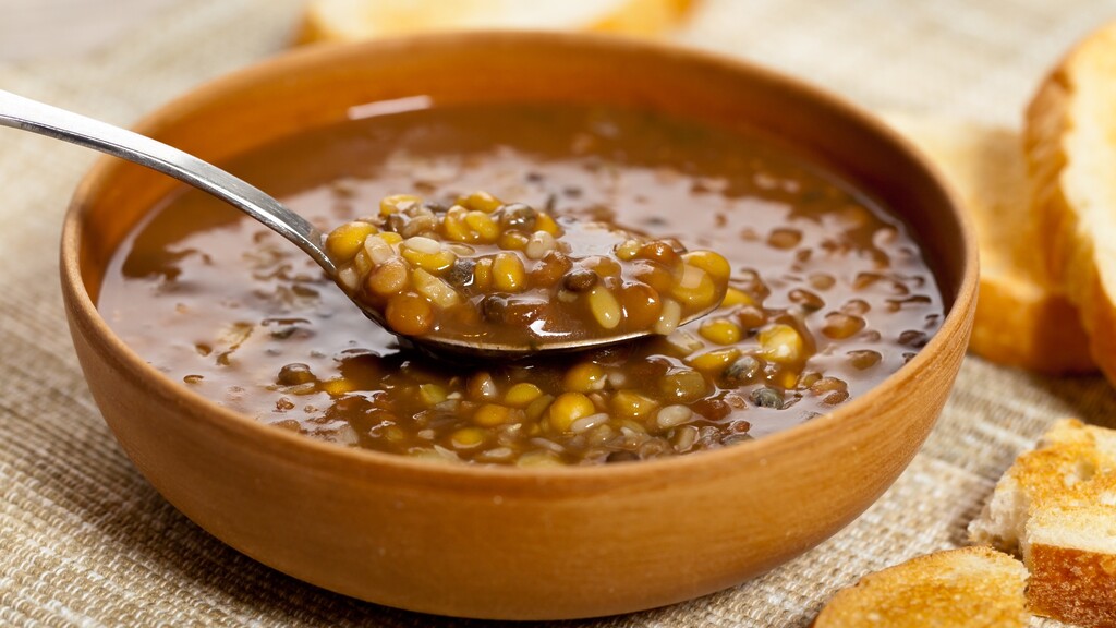 Warm lentil stew in a brown bowl with a spoon and toasted bread on the side.