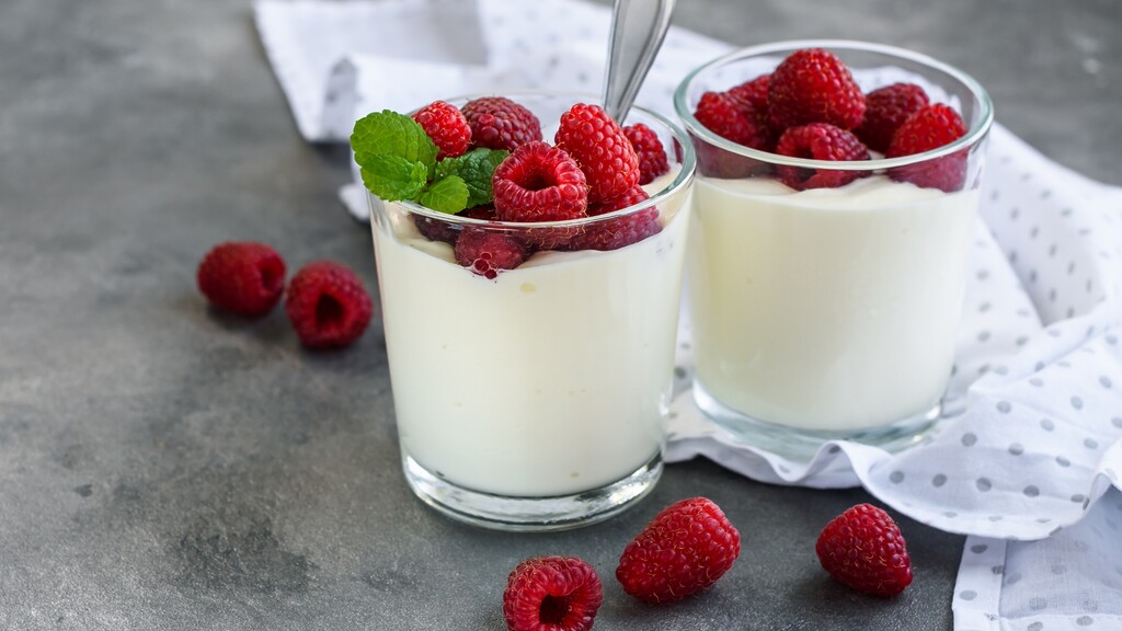 Plain yogurt topped with fresh raspberries in small glass cups.
