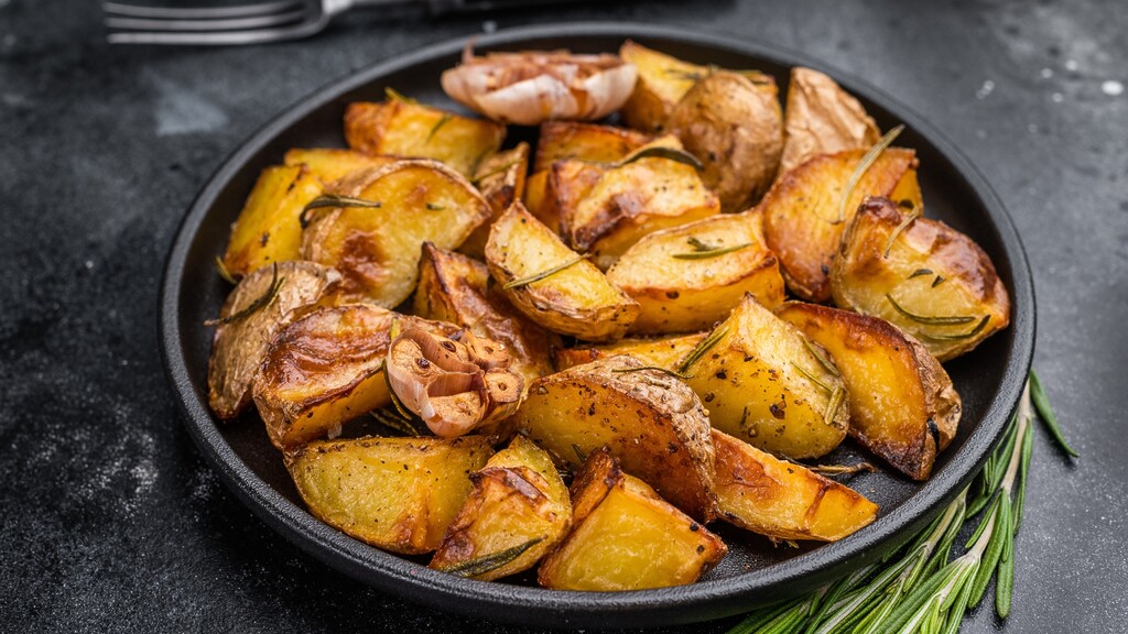Roasted potatoes with rosemary and garlic served in a black pan on a dark kitchen surface.
