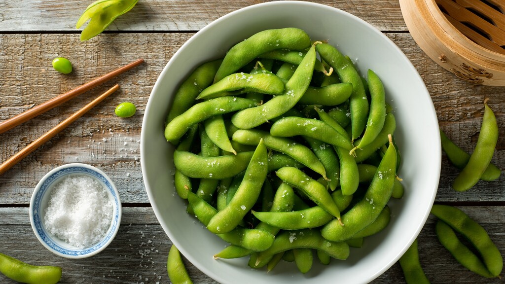 Steamed edamame pods sprinkled with sea salt in a white bowl.