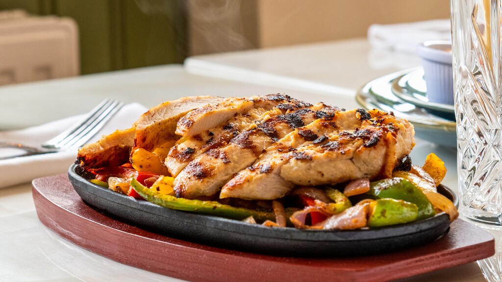 Grilled chicken strips served on a sizzling skillet with bell peppers and onions at a restaurant.