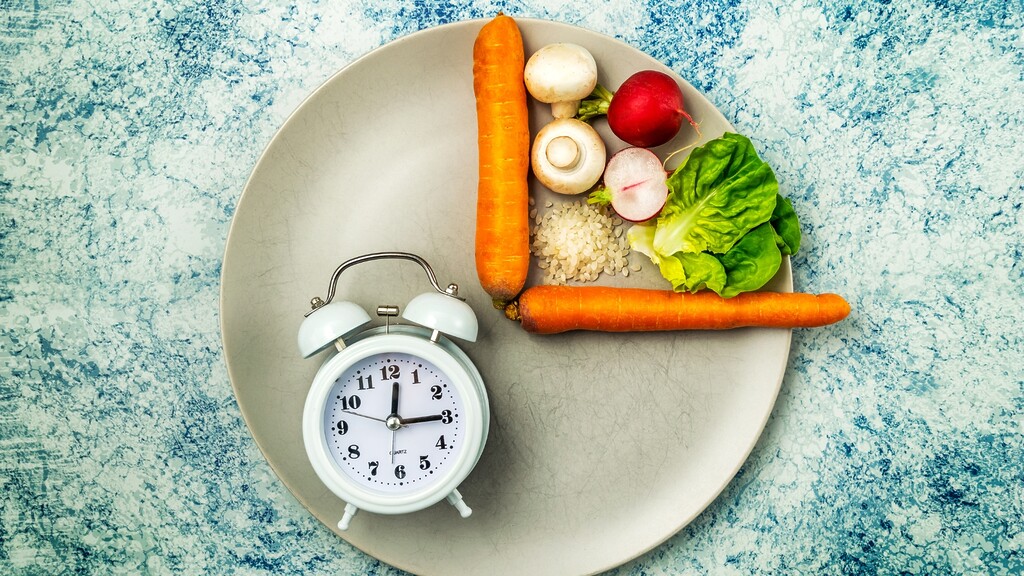Alarm clock on a plate with vegetables, illustrating meal timing and intermittent fasting.