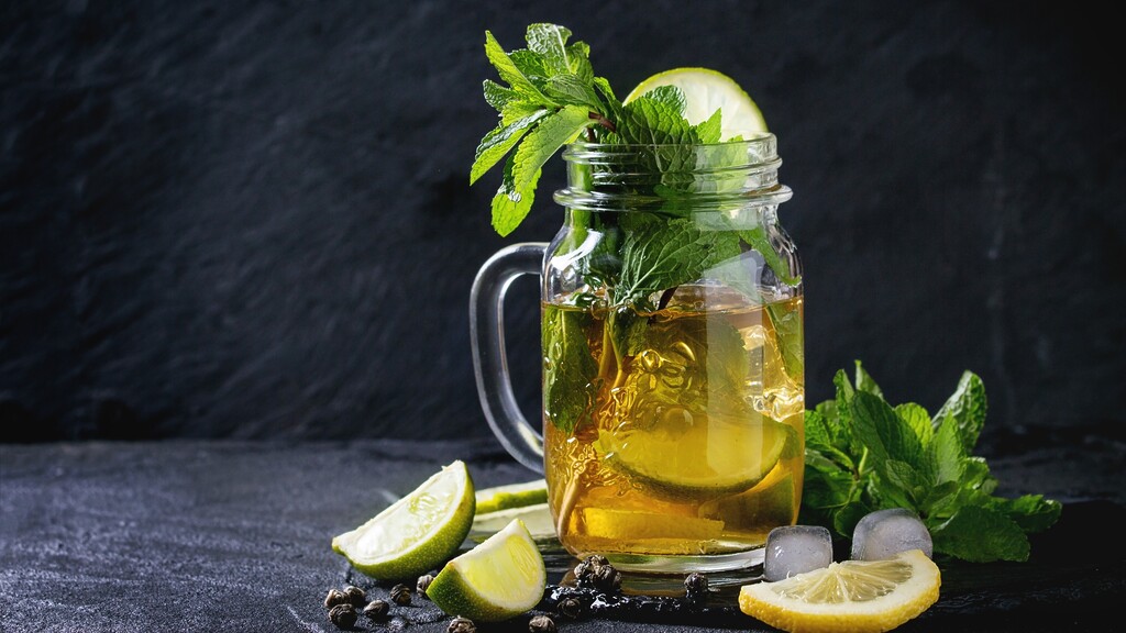 Iced green tea with lemon, lime, mint, and ice in a glass mason jar.