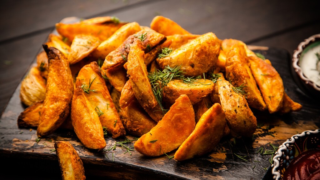 Crispy roasted potato wedges with fresh dill on a rustic wooden board.