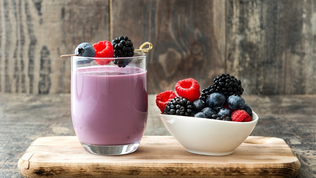 Berry smoothie with fresh blueberries, raspberries, and blackberries on a wooden board.