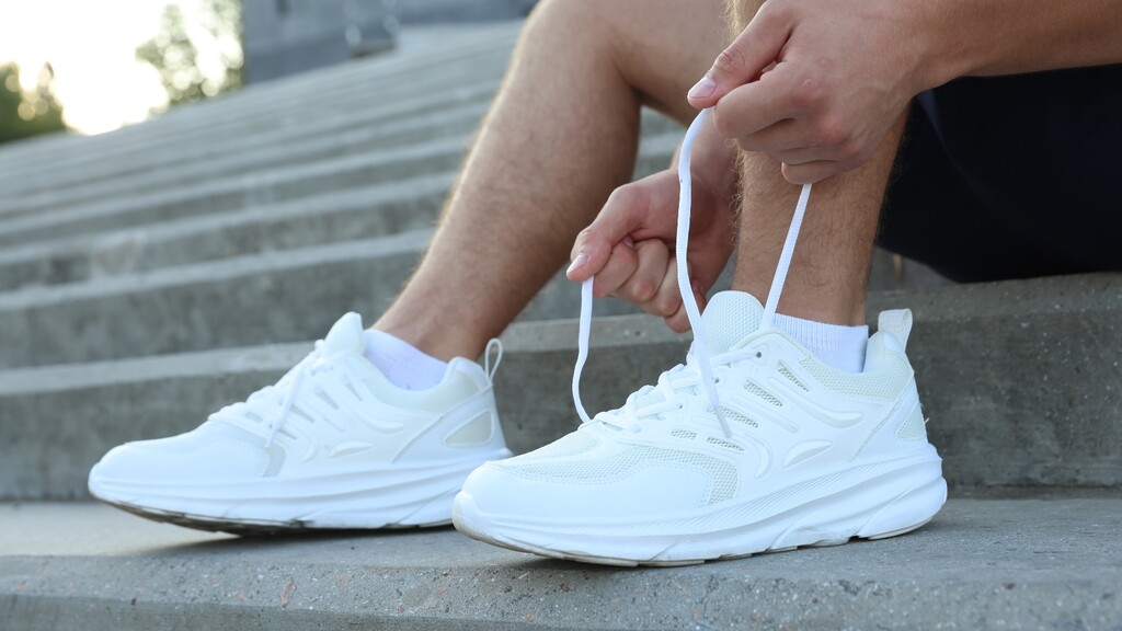 Man tying white walking shoes on outdoor steps before exercise.