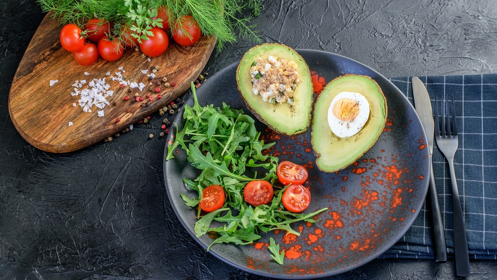 Avocado halves served with egg, greens, and cherry tomatoes on a plate.