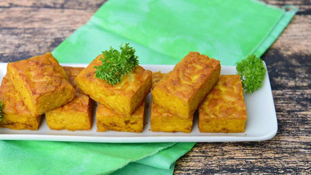 Golden baked tempeh blocks served on a white plate with fresh parsley.