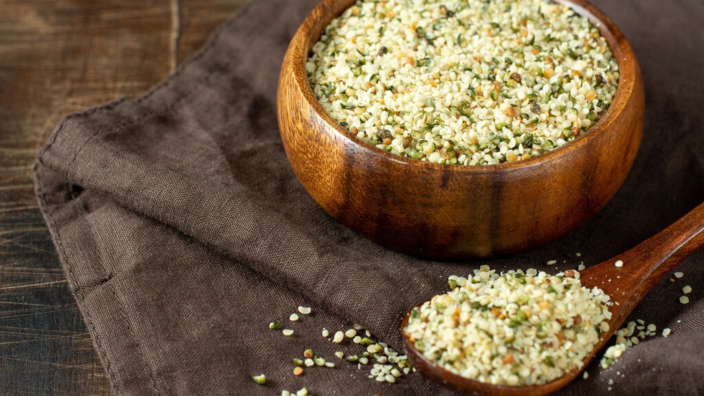 Hemp hearts in a wooden bowl and spoon on a rustic cloth.