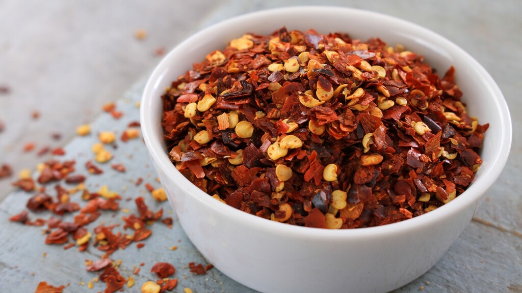 Crushed red pepper flakes in a white bowl with scattered flakes on the table.