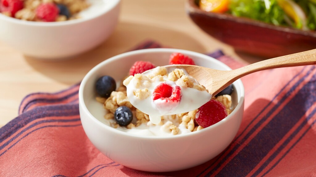 Greek yogurt with berries and granola on a wooden spoon over a breakfast bowl.
