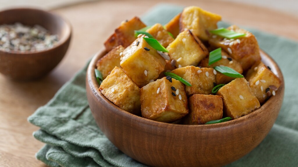 Crispy tofu cubes topped with sesame seeds and green onions in a wooden bowl.
