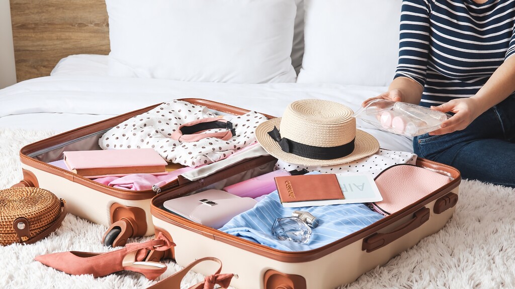 Open suitcase packed with travel clothes and a clear toiletry pouch, showing organized travel preparation.