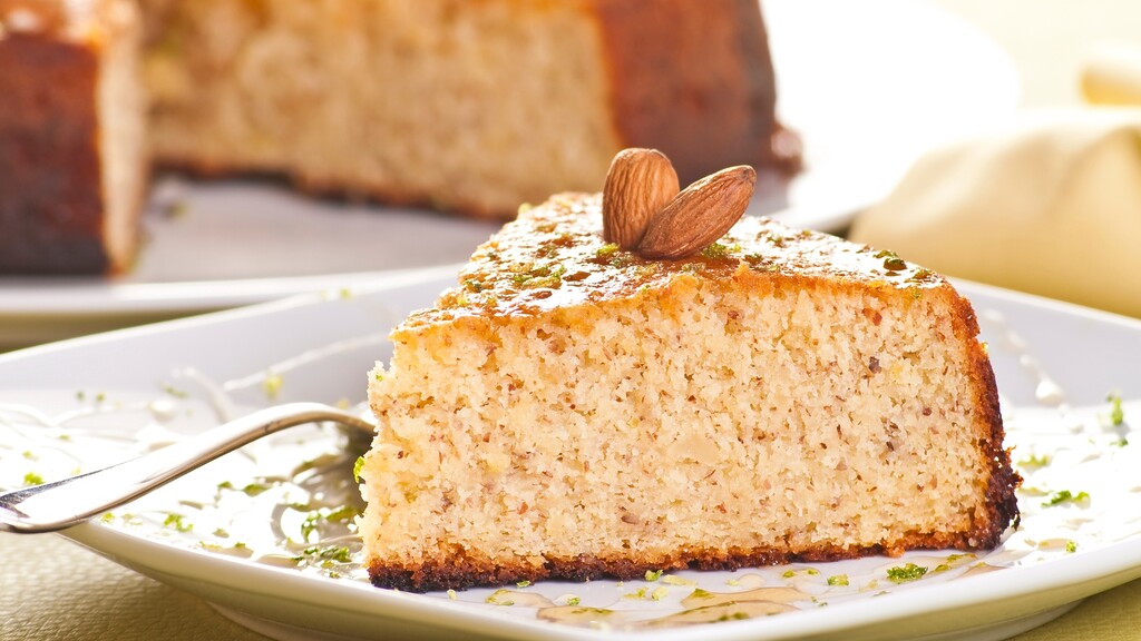 Slice of almond flour cake with a soft crumb, topped with almonds on a white plate.