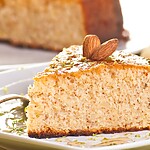 Slice of almond flour cake with a soft crumb, topped with almonds on a white plate.