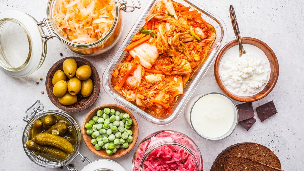 Overhead view of fermented foods including kimchi, sauerkraut, pickles, kefir, yogurt, and other probiotic-rich foods on a light surface.