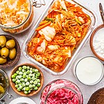 Probiotics for Diabetics: How Gut Health Impacts Blood Sugar Overhead view of fermented foods including kimchi, sauerkraut, pickles, kefir, yogurt, and other probiotic-rich foods on a light surface.