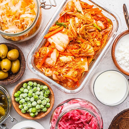 Overhead view of fermented foods including kimchi, sauerkraut, pickles, kefir, yogurt, and other probiotic-rich foods on a light surface.