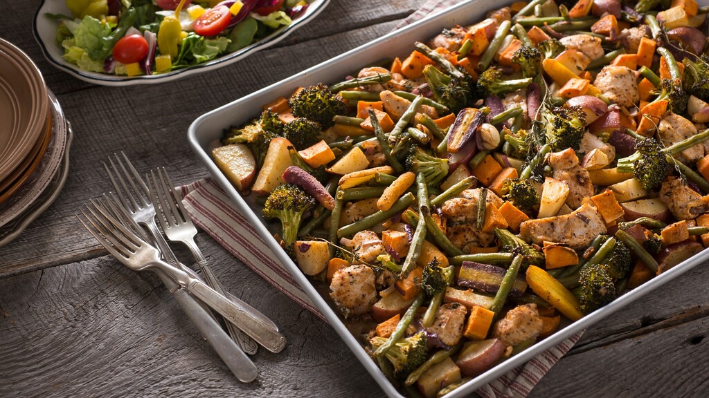 Sheet pan dinner with roasted chicken, broccoli, green beans, onions, and sweet potatoes on a rustic wooden table.