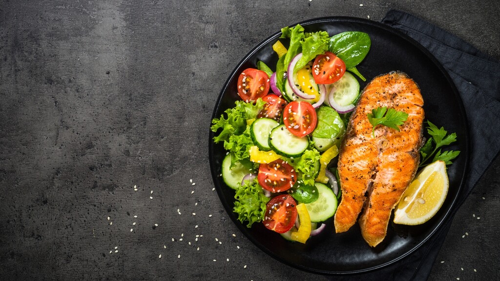 Salmon fillet served with a fresh vegetable salad on a dark plate.