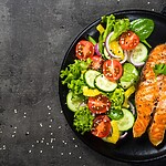 8 Natural Ways to Lower Blood Sugar (Without Total Deprivation) Salmon fillet served with a fresh vegetable salad on a dark plate.