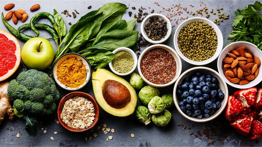 Assorted fiber-rich foods including leafy greens, almonds, avocado, broccoli, berries, seeds, oats, and legumes.