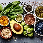 Assorted fiber-rich foods including leafy greens, almonds, avocado, broccoli, berries, seeds, oats, and legumes.