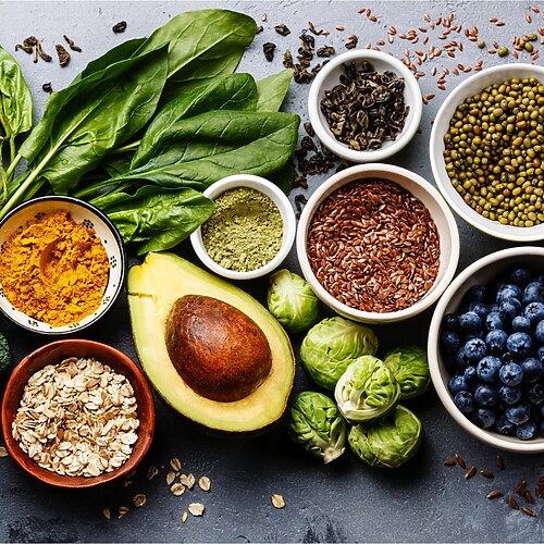 Assorted fiber-rich foods including leafy greens, almonds, avocado, broccoli, berries, seeds, oats, and legumes.