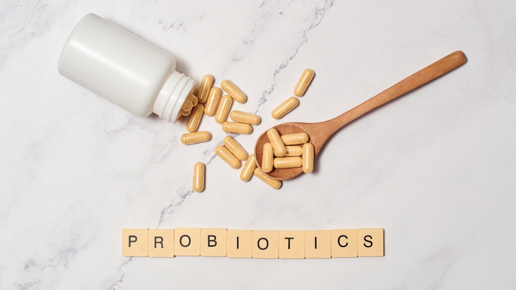 Probiotic capsules spilling from a bottle beside a wooden spoon, with the word probiotics spelled out on letter tiles.