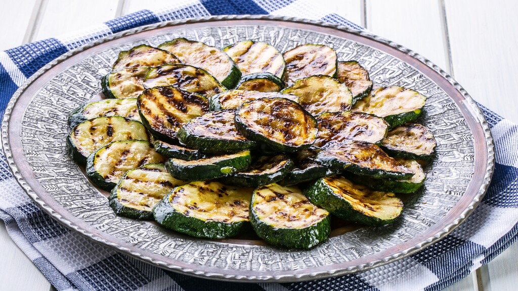 Grilled zucchini slices with char marks served on a patterned plate over a blue checkered towel.
